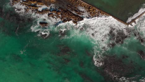 Aerial-drone-view-zooming-out-as-waves-rolling-in-crashing-over-rocks