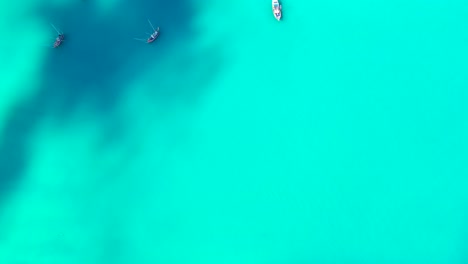 Turquoise-sea-texture-with-abstract-patterns-of-seabed-under-calm-clear-water-of-lagoon-with-floating-boats-in-Seychelles