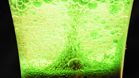 Makroaufnahme-Funkelnder-Grüner-Blasen,-Die-Sich-In-Einem-Glas-Mit-Hellem-Hintergrund-Nach-Oben-Bewegen-Und-Einige-Größere-Blasen-Heruntertropfen