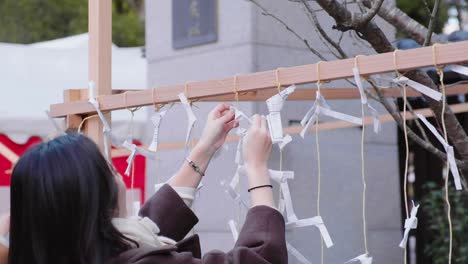 Japanisches-Mädchen-Hängt-Papiernotiz-An-Einem-Seil,-Das-An-Einem-Holzrahmen-Am-Yasaka-Schrein-In-Kyoto,-Japan,-Befestigt-Ist