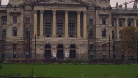 Üppiges-Gras-Und-Menschen,-Die-Vor-Dem-Historischen-Museum-Für-Ethnographie-In-Budapest,-Ungarn,-Mit-Auf-Der-Rückseite-Errichtetem-Turmdrehkran-Spazieren-–-Panoramaaufnahme