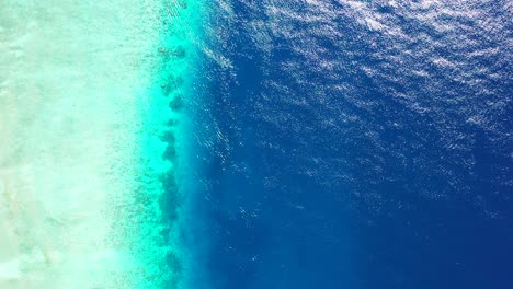 Deep-blue-sea-bordered-by-shallow-turquoise-lagoon-and-white-sandy-beach-seen-from-above-in-Maldives,-copy-space