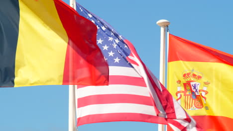 Cerrar-Banderas-Bélgica,-Estados-Unidos-Y-España-Ondeando-En-El-Viento,-Día-Soleado