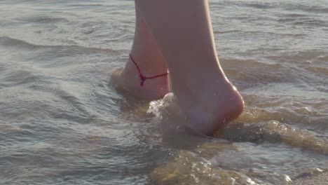 Slow-motion-close-up-of-female-feets-walking-into-waves-of-ocean-at-golden-hour