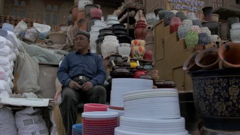 A-man-sitting-and-waiting-for-people-to-buy-his-handmade-clay-and-ceramic-jars-in-Kashgar,-Xinjiang-province-China---Wide-shot