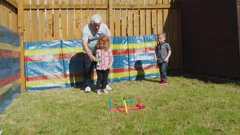 Grandfarther-playing-a-game-with-granddaughter-in-the-back-garden-as-a-small-boy-watches-them-during-summertime