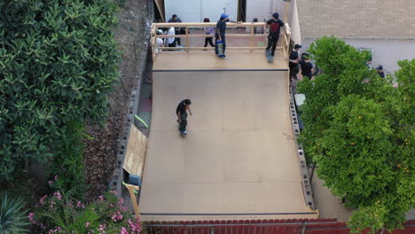 Skaters-riding-boards-on-Los-Angeles-backyard-skate-ramp,-aerial-view