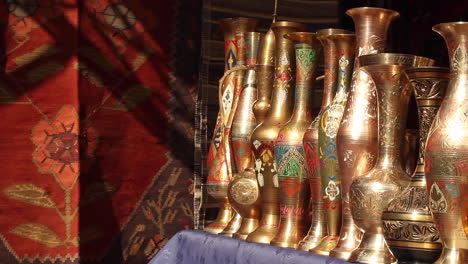 Row-of-ornate-gold-plated-vases-lined-in-market-next-to-handmade-rug-in-Yerevan,-Armenia