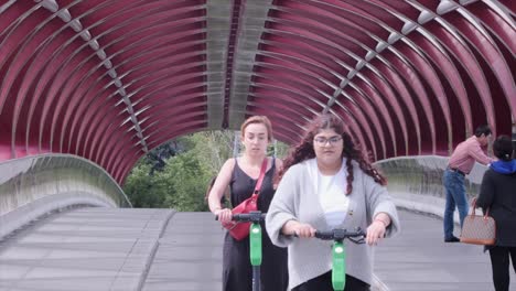 Peace-Bridge:-Two-young-women-ride-scooters-on-modern-urban-bridge