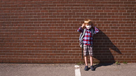Little-boy-standing-in-a-school-yard-puts-on-his-mask