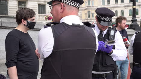 A-police-officer-makes-notes-during-a-stop-and-search-of-a-masked-environmental-activists-attending-a-Beyond-Politics-Party-protest-on-Trafalgar-Square