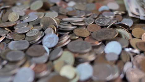 Close-up-on-coins-falling-on-pile-of-money,-selective-focus