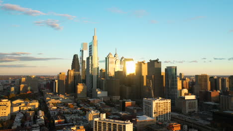 Rotating-aerial-drone-view-of-the-downtown-Philadelphia-skyline-featuring-tall,-glass-skyscrapers-at-sunset-with-golden-light-and-blue-summer-skies-showing-the-Comcast-Technology-Center