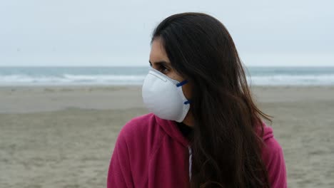 profile-portrait-of-casual-brunette-girl-with-Protective-Medical-Face-Mask-at-the-beach,-ocean-background,-relaxed,-thoughtful