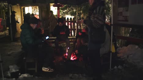 Gruppe-Japanischer-Menschen,-Die-In-Einer-Verschneiten-Nacht-In-Kyoto,-Japan,-Am-Kamin-Am-Kifune-Jinja-Schrein-Sitzen-Und-Sich-Warm-Halten