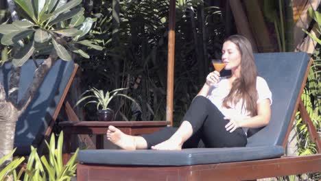 Medium-Shot-of-a-Young-Lady-Relaxing-on-a-Sun-Lounger-by-the-Pool-Drinking-a-Cocktail-at-a-Tropical-Hotel
