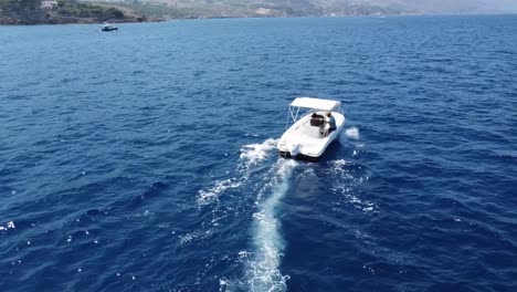Two-Men-Riding-A-Speedboat-And-Cruising-At-The-Deep-Blue-Sea-Near-The-Coastal-Village-Of-Scopello,-Sicily,-Italy-During-Summer