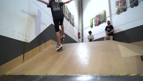 Slow-motion-shot-of-skateboarder-riding-up-the-ramp-doing-kickflip-trick-and-driving-down