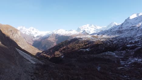 Drone-view-of-a-swiss-valley-with-the-snow-capped-alps-in-the-background,-sunny