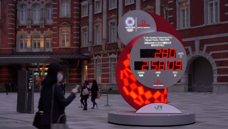Tokyo-Olympic-Games-countdown-clock-with-commuters-wearing-facemasks-passing-through-frame-during-Corona-Crisis-2020