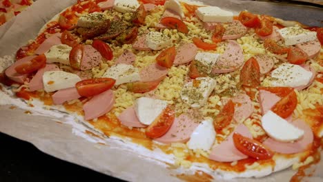 Female-home-cook-is-pouring-fresh-spices-on-homemade-pizza-with-mozzarella-and-tomatoes