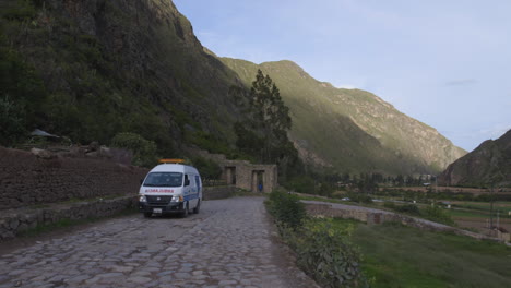 An-ambulance-driving-along-a-cobblestone-street-that-leads-to-Ollantaytambo-in-Peru's-Sacred-Valley