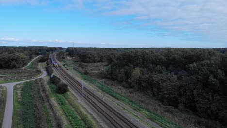 Dutch-train-passing-on-a-railway-track-on-a-summer-day-in-the-netherlands,-Drone-shot