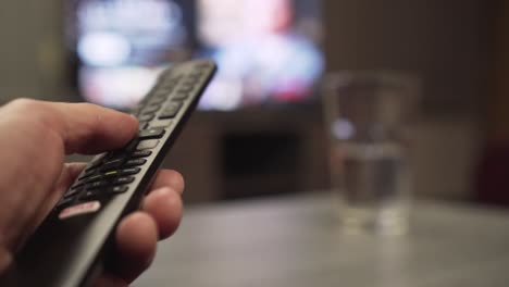 Male-hand-holding-TV-remote-control-and-pushing-Netflix-button,-extreme-closeup,-blurry-screen-in-background