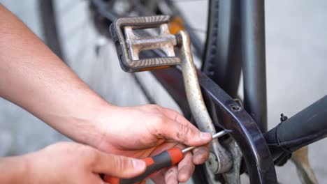 Caucasian-male-mechanic-hand-uses-screwdriver-to-loosen-screw-on-bicycle-pedal,-above-close-up-static