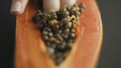 Close-up-of-female-fingers-diving-into-the-seeds-of-papaya-cut-in-half