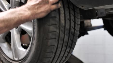 Wheel-tire-analyzed-by-car-mechanic,-car-chassis-on-jack-lift-in-garage