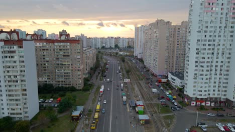 Aerial-view-overlooking-cars-on-a-avenue,-between-old-apartment-building,-during-sunset,-in-Troieshchyna-neighborhood-of-Kiev,-Ukraine---reverse,-drone-shot