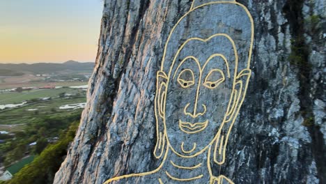 4k-Close-up-Aerial-view:-image-of-Buddha,-sitting-cross-legged,-engraved-with-gold-into-the-northern-face-of-a-limestone-hill-in-Khao-Chi-Chan,-Thailand