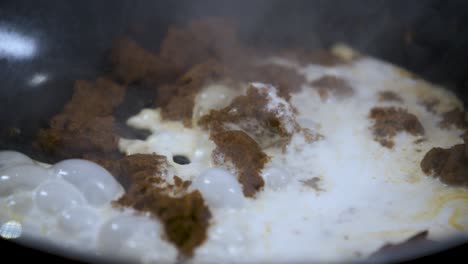 Gießen-Sie-Weiße-Kokosmilch-Mit-Trockener-Thailändischer-Brauner-Currypaste-In-Eine-Brutzelnd-Heiße-Schwarze-Pfanne