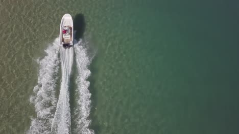 Top-down-aerial-of-white-speed-boat-wake-in-shallow-sunny-green-lagoon
