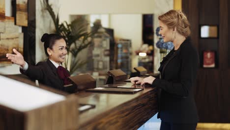 Female-Receptionist-In-An-Asian-Hotel-Handing-Over-Door-Key-Of-A-Hotel-Room-To-A-Businesswoman---medium-shot,-slow-motion