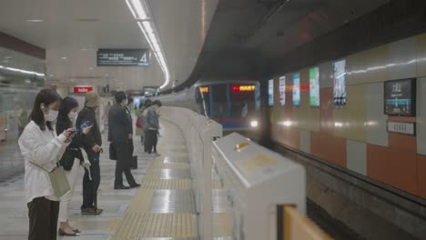 Der-Jr-Zug-Kommt-Mit-Menschen-Mit-Gesichtsmasken-An,-Die-Auf-Dem-Bahnsteig-Des-Bahnhofs-In-Tokio,-Japan,-Stehen