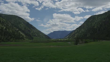 4K-Zeitraffer-Eines-Feldes-Mit-Bergen-Mit-Grünen-Feldern,-Weißen-Wolken-Und-Ranch