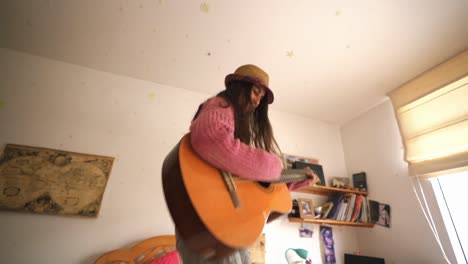 Junges-Mädchen-Springt-Mit-Gitarre-Im-Schlafzimmer-Zu-Hause-Auf-Das-Bett
