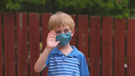 Cute-little-boy-waving-while-wearing-a-protective-face-mask