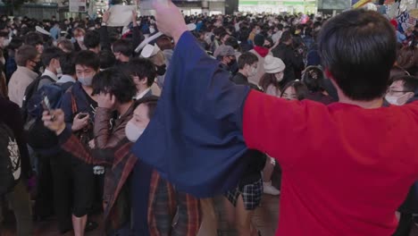 A-Guy-In-Red-Shirt-With-Ruffles-Not-Wearing-Mask-Performing-In-Front-Of-The-Busy-Crowd-On-Halloween-Night-At-Shibuya-Crossing-In-Tokyo,-Japan---Slow-Motion