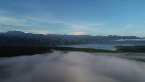 Fog-to-landscape-revelation-aerial-view-of-mountains-and-lake-in-the-Caribbean,-then-pan-down-to-dark-forest-area