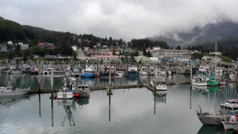 Barcos-Y-Yates-Amarrados-En-Aguas-Tranquilas-Con-Estructuras-En-El-Paisaje-Montañoso-Del-Bosque-Al-Fondo-En-Alaska,-Ee.uu.