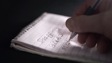 Hand-writing-shopping-list-on-notepad-for-essentials-close-up-shot