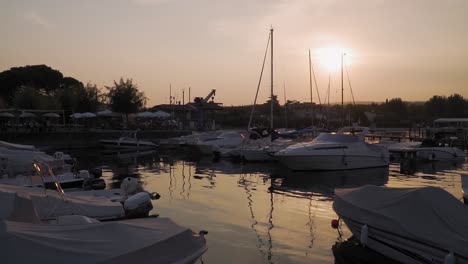 Boote-In-Einem-Kleinen-Yachthafen-Am-Gardasee-Bei-Sonnenuntergang,-Friedliche-Zeitlupenansicht-Des-Sonnenuntergangs