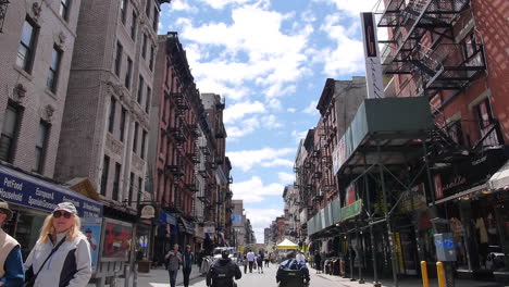 Zwei-Männer-Im-Rollstuhl-Bewegen-Sich-Die-New-Yorker-Straße-Entlang,-Die-Kamera-Schwenkt-Nach-Oben,-Ein-Fliegender-Vogel-Im-Sonnenlicht,-Totale