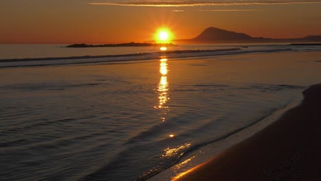 Rising-sun-reflecting-in-shallow-ocean-waves,-calm-sea-beach-sunrise,-mediterranean,-spain