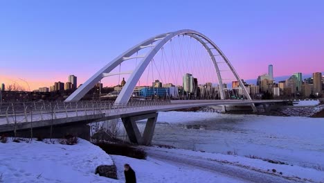 Twilight-Sunset-Time-Lapse-4k-accented-by-white-modern-Walter-Dale-Bridge-with-a-stunning-horizon-in-Blue-Purple-Pink-Orange-and-people-walking-alone-masked-respecting-random-others-walking-closeby