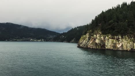 Rocky-gray-island-covered-with-green-trees-in-the-Trincomali-channel-on-a-cloudy-rainy-day-in-Canada