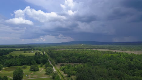 Slow-pan-left-to-right-aerial-shot-of-a-rural-summertime-landscape-and-farm-land-with-storm-clouds-in-the-distance